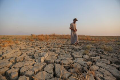 A fisherman walks across a dry patch of land after drought in the marshes of southern Iraq, Dhi Qar province. Image ID: 2M9TRTP.